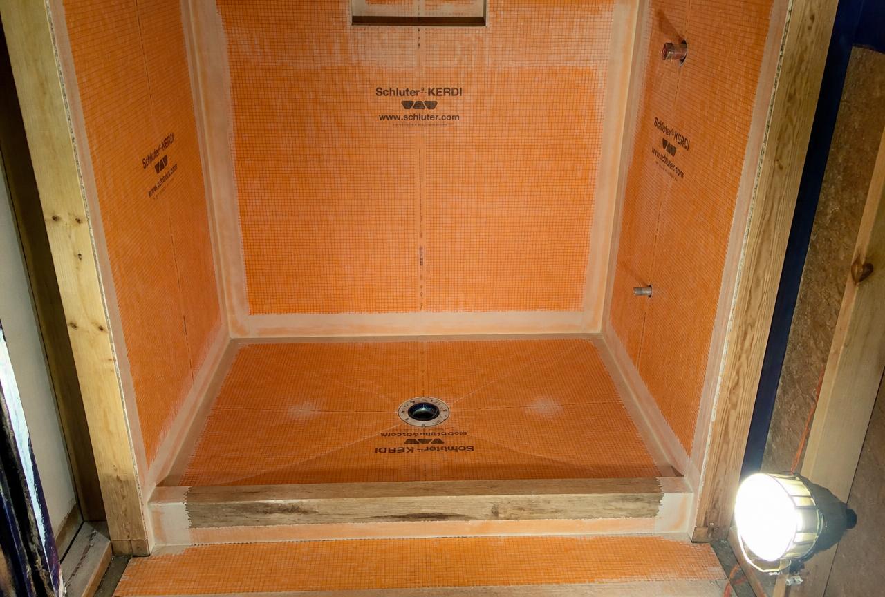 Rebuilt shower pan in a Nampa, Idaho bathroom at the waterproofing stage, with bonded orange membrane, banded corners and a bonding-flange drain before tile