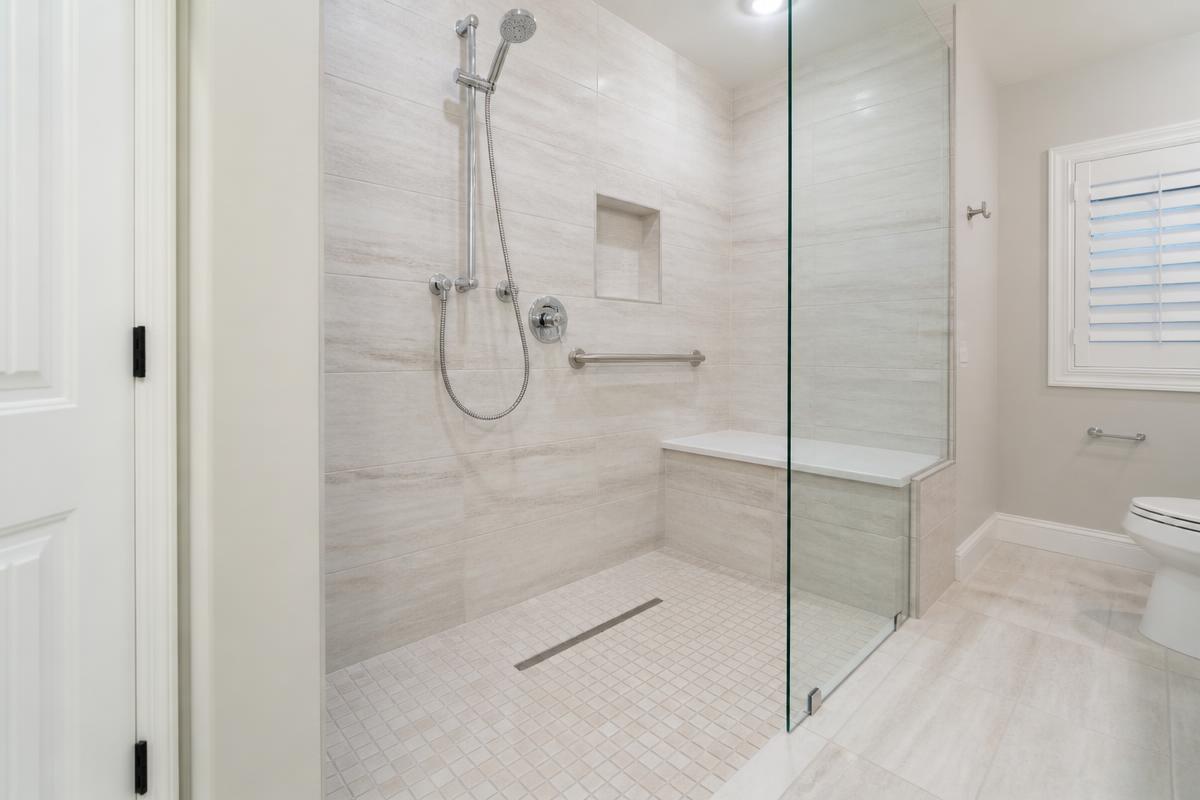 Curbless walk-in shower in a Nampa, Idaho home with a tiled bench, linear drain, grab bar and handheld sprayer